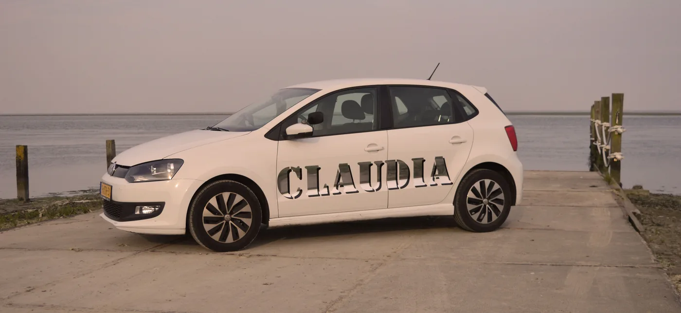 Witte lesauto met Claudia-belettering, geparkeerd aan het water